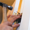hammer driving a whittled piece of scrap wood into a stripped screw hole to repair a loose hinge