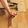 using a pry bar to remove a piece of flooring to check its thickness