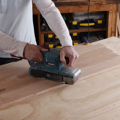 sanding the side of a storage chest with a belt sander