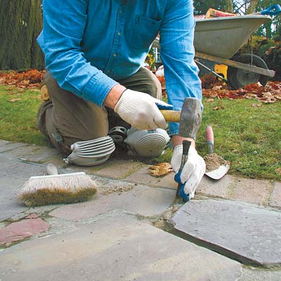 chiseling out the crumbling mortar in a cracked stone walkway