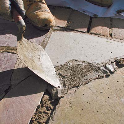 troweling the fresh mortar into joints in a stone walkway