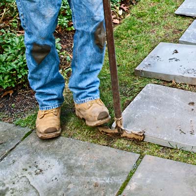 using a half-moon edger to cut around base of each paver in stone stepping path 