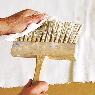 wiping excess glaze from the stiff-bristled brush with a clean rag