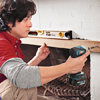 photo of support ledge install using a drill and level to secure a 1x3 to the top of the fireplace surround