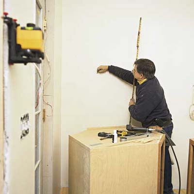 tom silva marking the reference lines on the wall before installing kitchen cabinets