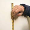 tom silva measuring with a measuring tape, and marking layout line of the wall with a pencil
