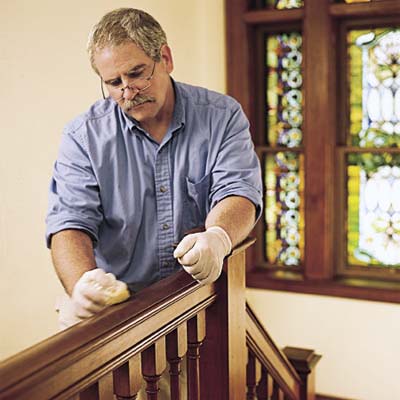 man waxing and buffing the wooden stair rail with furniture wax