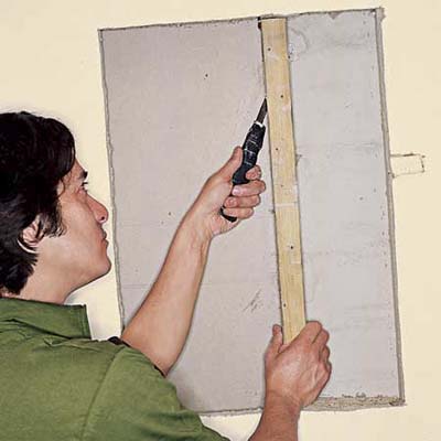 Cutting through drywall screws with a hacksaw blade, wrapped in tape at the end for a handle.